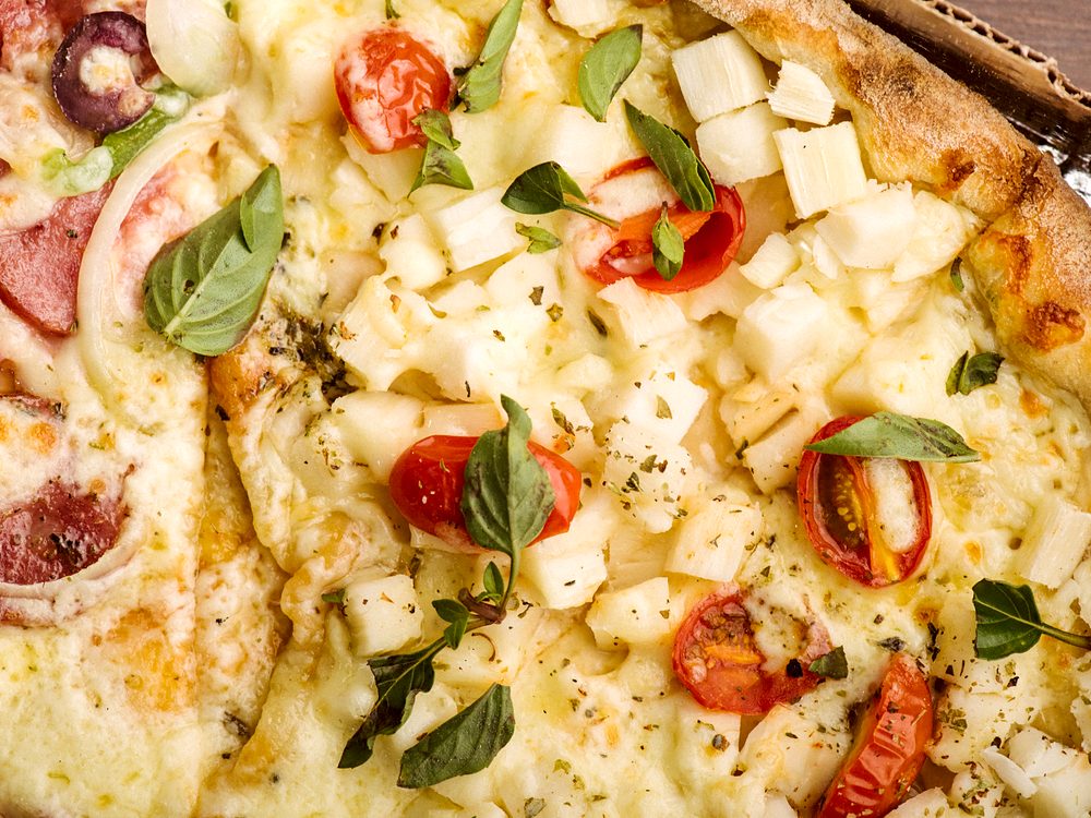 Pizza com tomate-cereja, manjericão e queijo, em close