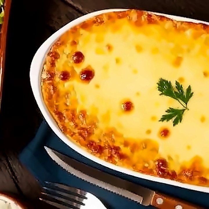 Escondidinho gratinado na travessa branca, com salada de tomate ao lado