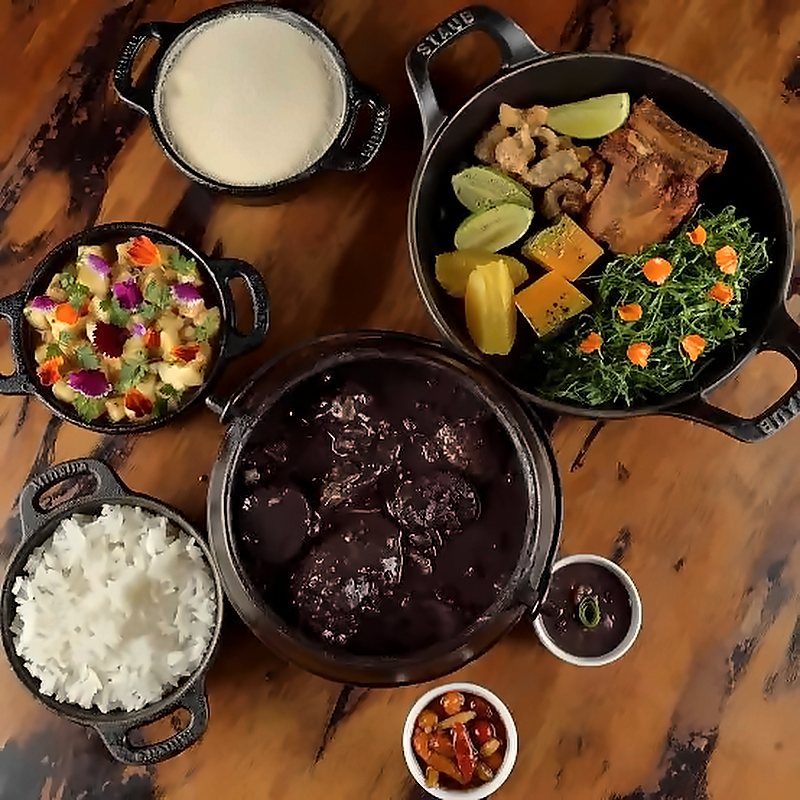 Mesa de feijoada vista de cima, com a panela de feijão, arroz, couve, farofa e acompanhamentos