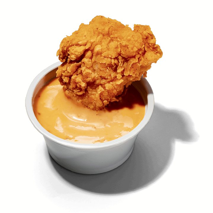 Pote de molho Nola com um pedaço de frango empanado