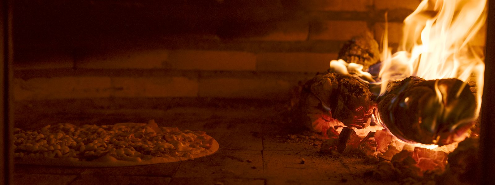 Pizza assando no forno a lenha, ao lado do fogo